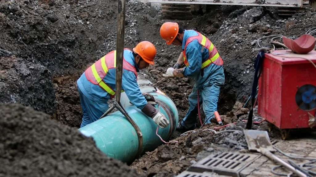 Workers installing heavy-duty municipal piping for a water system supported by a 10 inch submersible pump.