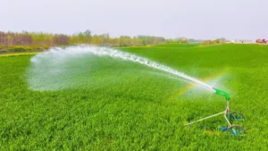 A large-scale green field being watered by a powerful traveling sprinkler system connected to a High-Flow Pump.